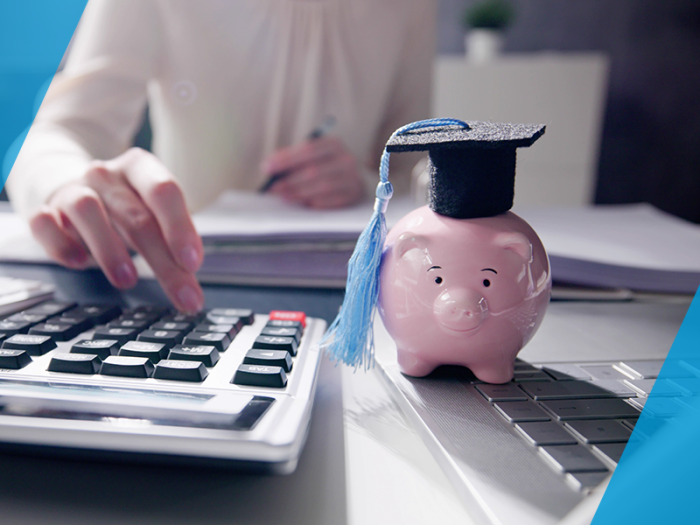 piggy bank sitting on desk wearing graduation cap next to calculator